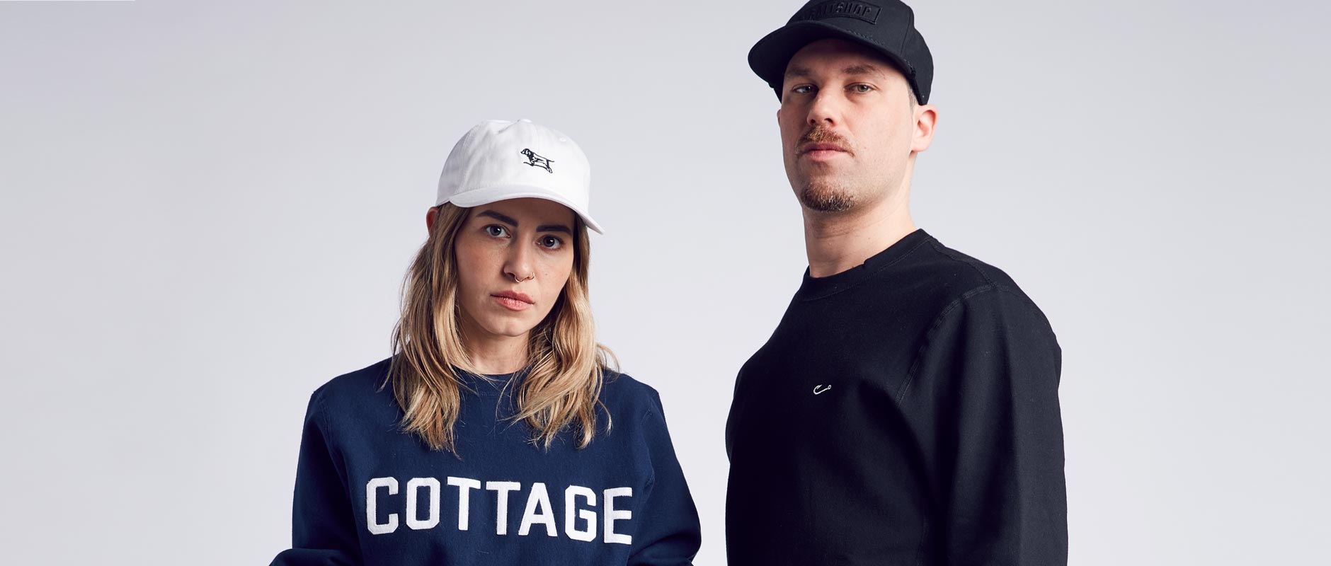 Female model wearing Baitshop Hunting Dad Hat and Cottage Crew neck beside Male model wearing Black Embroidered Hook Crewneck